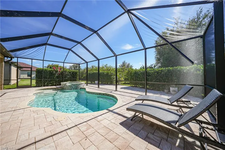 View of pool featuring glass enclosure, a pool with connected hot tub, and a patio area