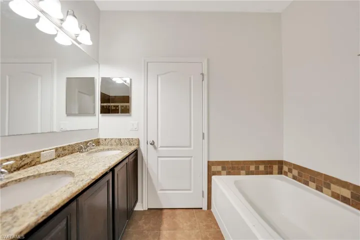 Full bath with double vanity, a bath, tile patterned flooring, and a sink