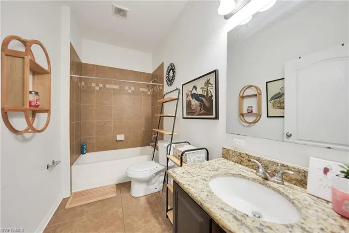 Bathroom featuring visible vents, washtub / shower combination, toilet, vanity, and tile patterned flooring
