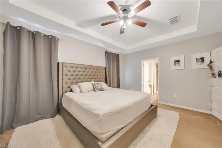 Bedroom featuring visible vents, baseboards, a ceiling fan, light carpet, and a tray ceiling