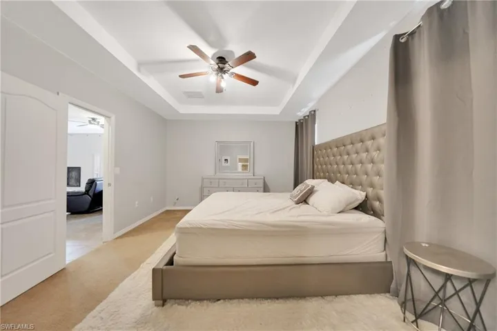 Bedroom featuring a raised ceiling, baseboards, light colored carpet, visible vents, and ceiling fan