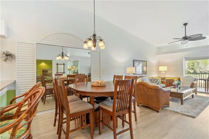 Dining space featuring ceiling fan with notable chandelier, light wood-type flooring, and vaulted ceiling