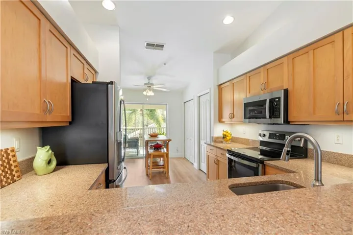 Kitchen with light stone countertops, ceiling fan, sink, stainless steel appliances, and vaulted ceiling