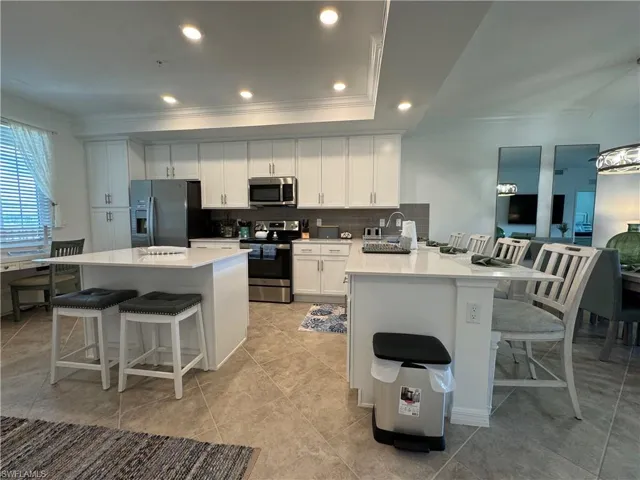 Kitchen with white cabinetry, appliances with stainless steel finishes, kitchen peninsula, light tile patterned floors, and a breakfast bar
