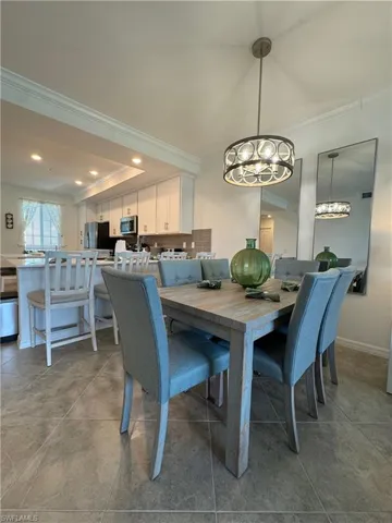 Tiled dining area with a notable chandelier, a raised ceiling, and ornamental molding