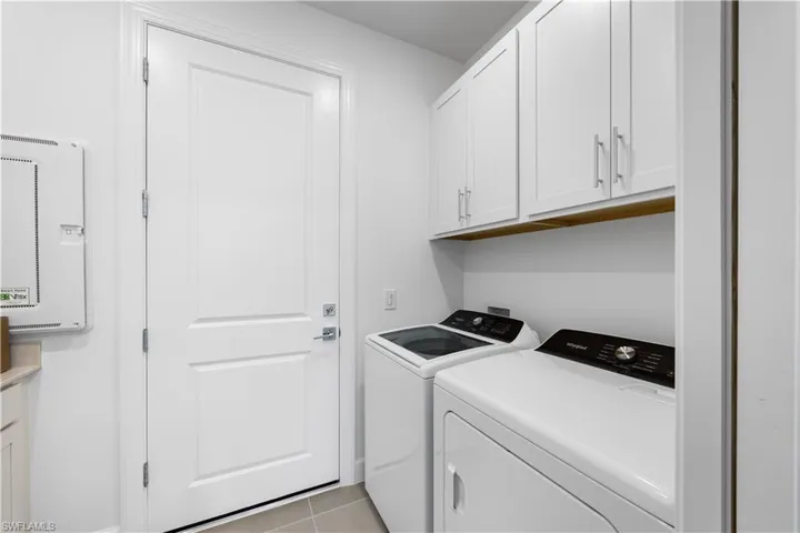 Laundry area featuring white cabinetry with silver hardware, an integrated wood-finish shelf, and light-toned floor tiling