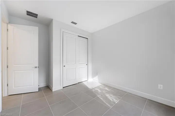Room featuring light gray walls, gray tile flooring, a white paneled door, and white sliding closet doors