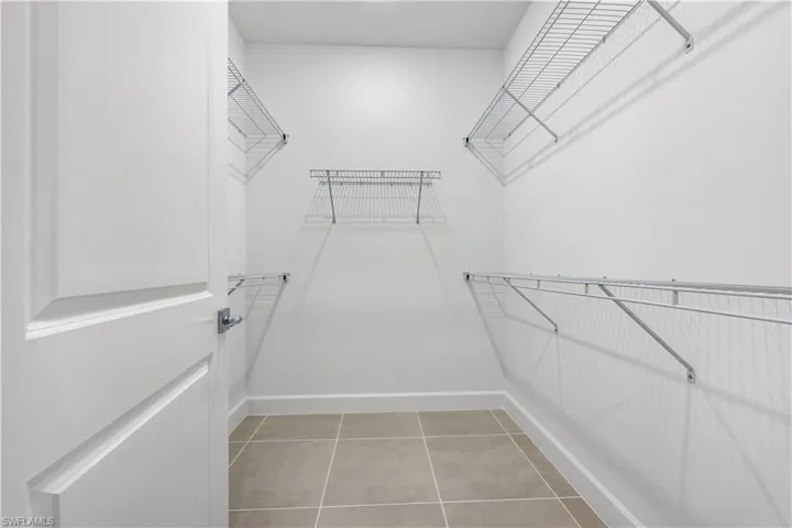 Walk-in closet featuring an open door, light-colored walls, tile flooring, and multiple wire shelving units