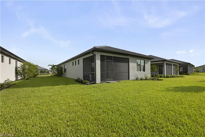 Expansive green lawn bordering the rear elevation featuring a screened lanai with dark screening, neutral stucco exterior, and a dark tile roof