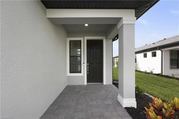 Covered entry featuring a dark paneled door with sidelight window, recessed lighting, paver walkway, and stucco exterior