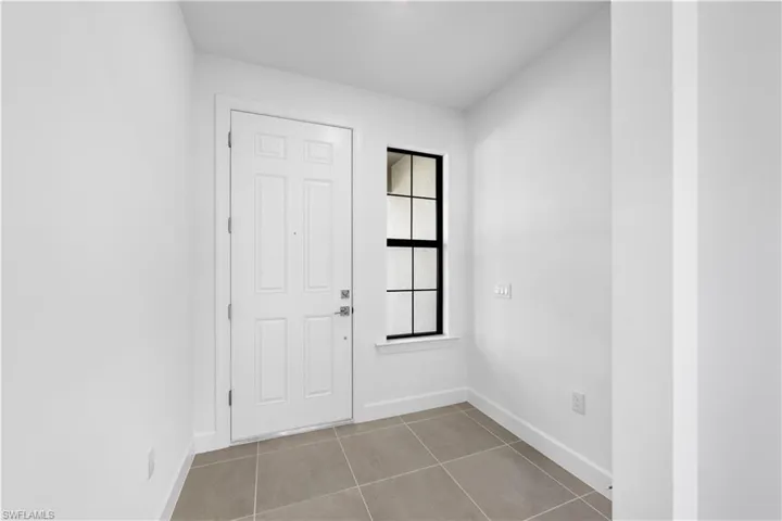 Entry foyer featuring neutral-toned tile flooring, a paneled entry door, and a multi-pane window with black framing