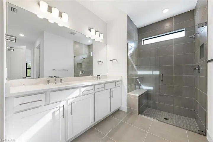 Spacious bathroom featuring a dual vanity with a light-toned countertop, a large frameless mirror, and modern light fixtures