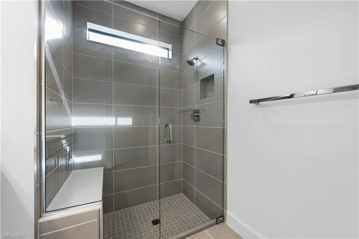 Walk-in shower featuring a frameless glass enclosure, floor-to-ceiling grey tile, a built-in shower niche, and an integrated bench