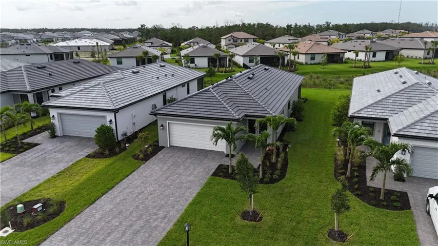 Contemporary home featuring a gray tile roof, paver driveway, attached garage, well-maintained lawn, and mature landscaping