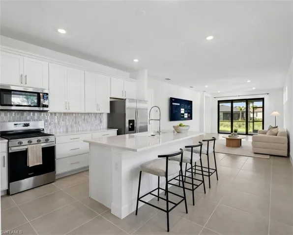 *Virtually Staged*Contemporary kitchen featuring white cabinetry, stainless steel appliances, a mosaic tile backsplash, and a large central island with seating