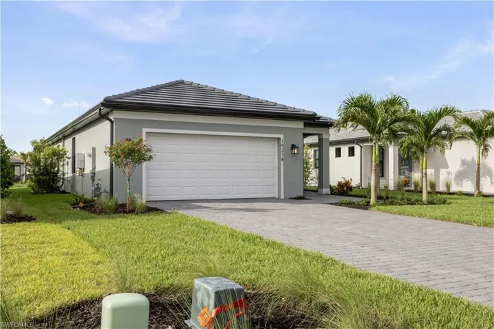 Contemporary home exterior featuring a paver driveway, an attached garage, a tile roof, and manicured landscaping with palm trees