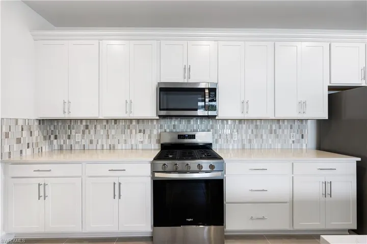 Kitchen featuring extensive white cabinetry, a mosaic tile backsplash, light-toned countertops, and stainless steel appliances including a gas range and built-in microwave