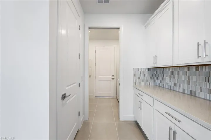 Contemporary kitchen featuring white cabinetry, light-toned countertops, and a mosaic tile backsplash