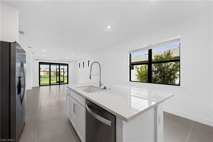Kitchen island featuring a single-basin sink with a gooseneck faucet, light-toned countertop, and integrated dishwasher