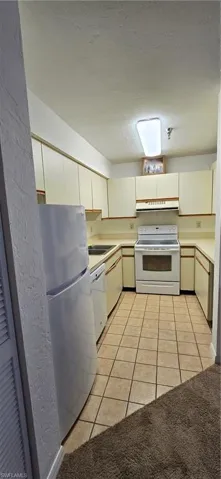Kitchen featuring range, light tile patterned floors, light countertops, white cabinetry, and white refrigerator