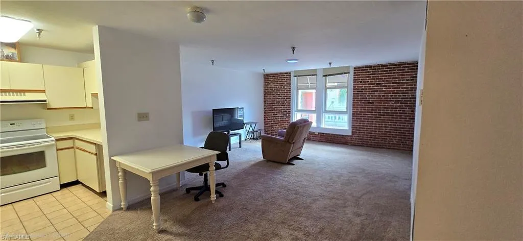 Kitchen with white electric stove, light countertops, brick wall, light colored carpet, and exhaust hood