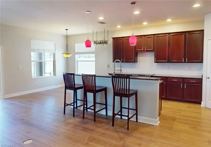 Kitchen with light hardwood / wood-style floors, tasteful backsplash, an island with sink, decorative light fixtures, and sink
