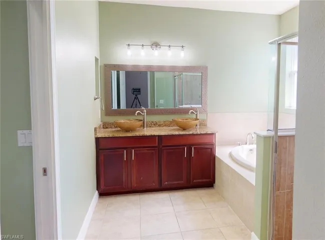 Bathroom featuring tile floors, tiled tub, and double vanity