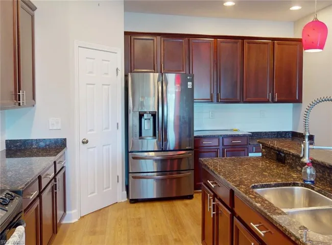 Kitchen with light hardwood / wood-style flooring, stainless steel appliances, hanging light fixtures, tasteful backsplash, and sink