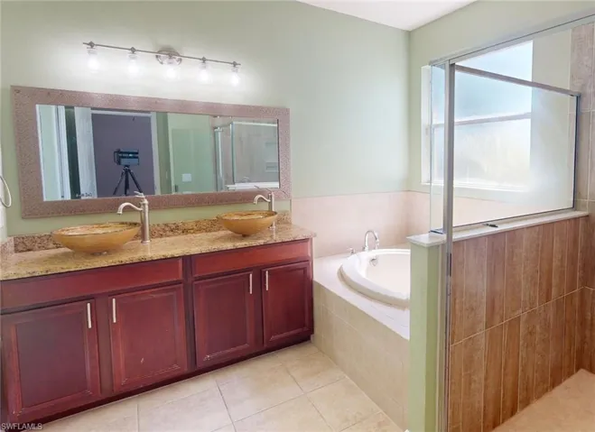 Bathroom featuring tile floors, independent shower and bath, and dual bowl vanity