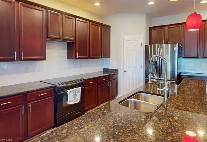 Kitchen with stainless steel fridge with ice dispenser, hanging light fixtures, tasteful backsplash, black range with electric stovetop, and sink