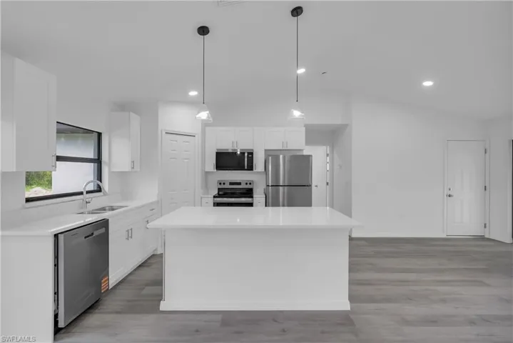 Kitchen with white cabinets, stainless steel appliances, vaulted ceiling, hanging light fixtures, and recessed lighting