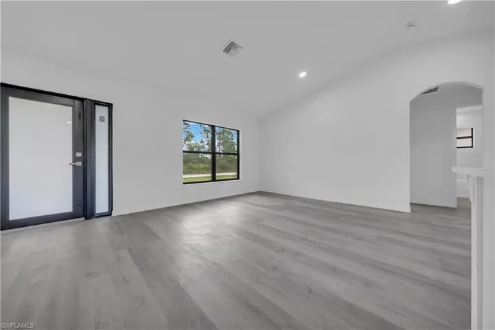 Empty room with vaulted ceiling, arched walkways, light wood-style flooring, and recessed lighting