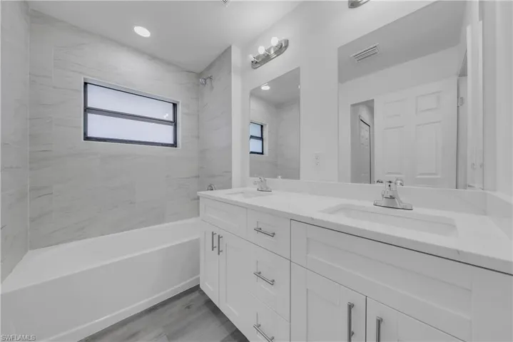 Bathroom with double vanity, washtub / shower combination, light wood finished floors, and recessed lighting