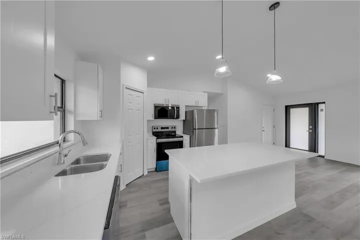 Kitchen with white cabinetry, stainless steel appliances, hanging light fixtures, a kitchen island, and light wood finished floors