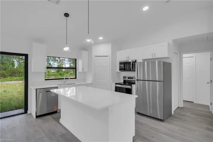 Kitchen with stainless steel appliances, white cabinets, hanging light fixtures, light stone counters, and a center island
