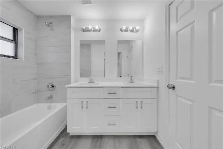 Bathroom with double vanity, light wood-style flooring, and shower / bath combination