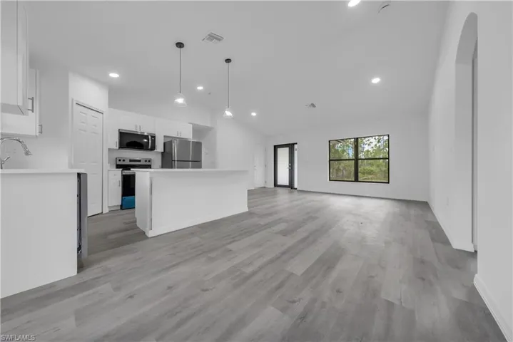 Kitchen with white cabinets, open floor plan, stainless steel appliances, vaulted ceiling, and light countertops