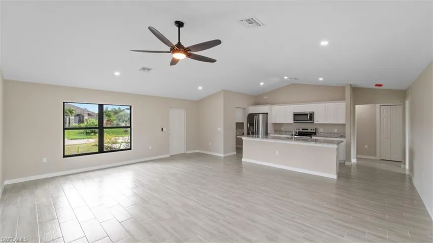 Kitchen with open floor plan, appliances with stainless steel finishes, a center island with sink, and white cabinets