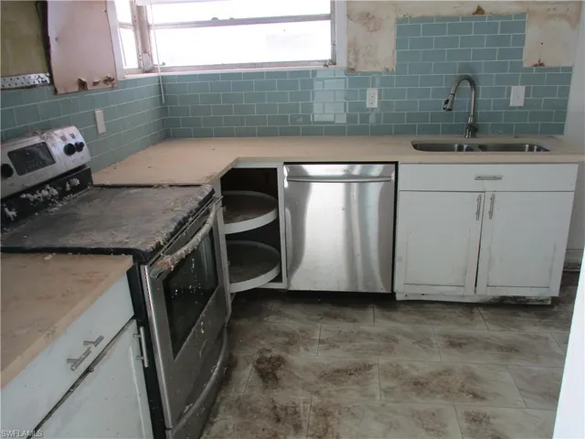 Kitchen featuring stainless steel appliances, decorative backsplash, white cabinetry, and light tile patterned floors