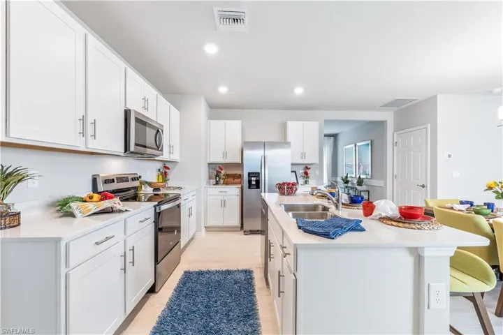 Kitchen with appliances with stainless steel finishes, white cabinetry, light wood-type flooring, a center island with sink, and sink