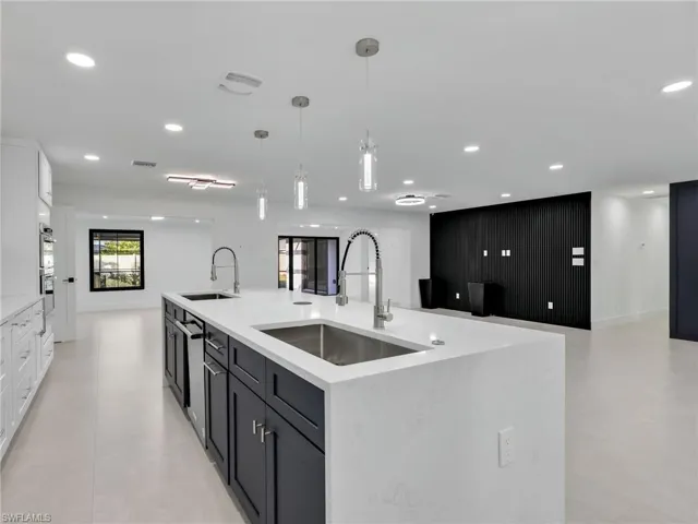 Kitchen with a spacious island, white cabinets, light stone countertops, hanging light fixtures, and open floor plan