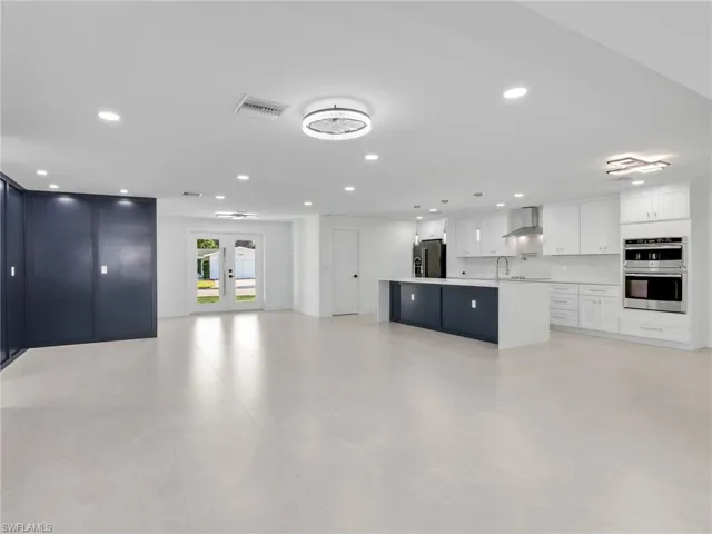 Kitchen featuring open floor plan, white cabinets, a spacious island, stainless steel double oven, and wall chimney range hood