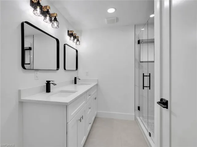 Full bath featuring double vanity, a marble finish shower, and light tile patterned floors