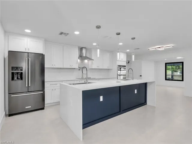 Kitchen with stainless steel appliances, white cabinets, a center island with sink, light stone countertops, and recessed lighting