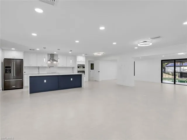 Kitchen featuring open floor plan, white cabinets, appliances with stainless steel finishes, a large island with sink, and recessed lighting