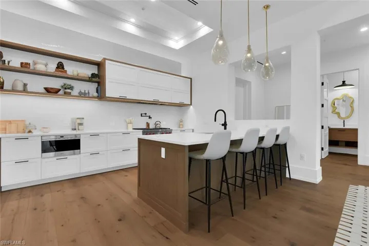 Kitchen with wood finished floors, white cabinets, a breakfast bar, light countertops, and a peninsula