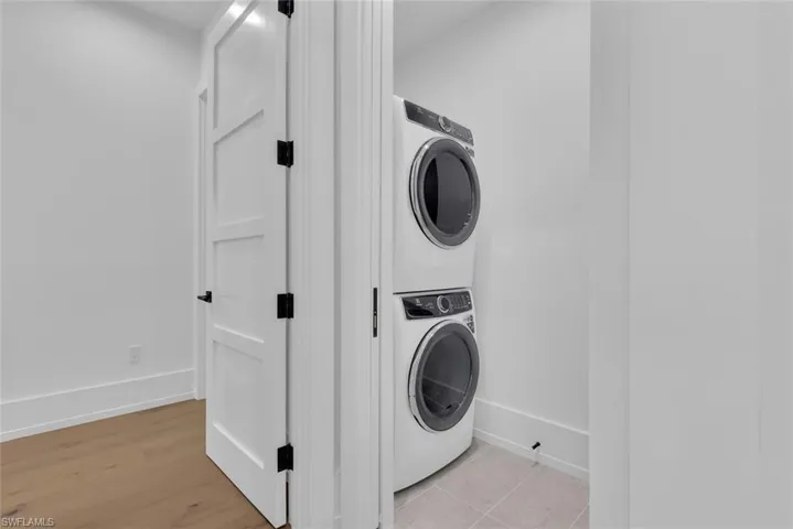 Clothes washing area featuring stacked washer / dryer, baseboards, and light wood finished floors