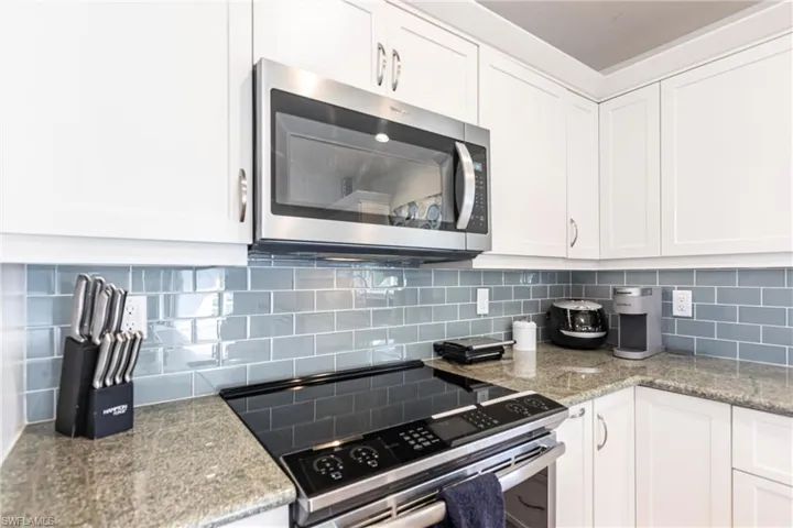 Kitchen featuring stainless steel appliances, white cabinetry, decorative backsplash, and light stone counters