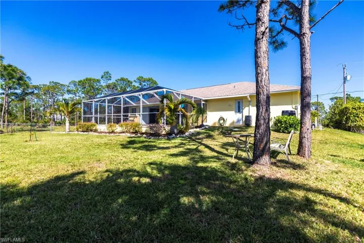 Rear view of property with a lawn, glass enclosure, and stucco siding