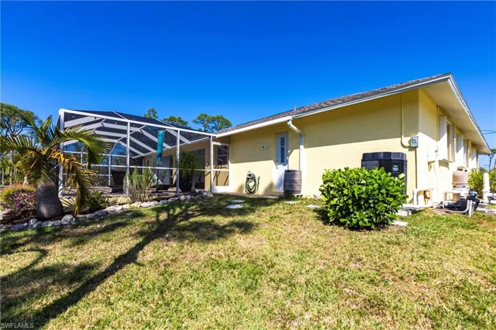Back of property with stucco siding, a lawn, and a lanai